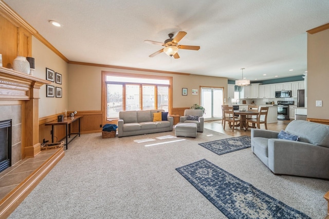 living area featuring a wainscoted wall, ornamental molding, recessed lighting, ceiling fan, and a tile fireplace