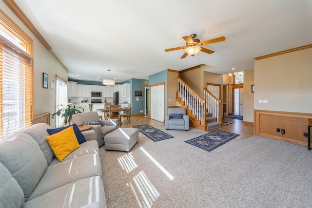 living area with stairs, crown molding, light carpet, and ceiling fan