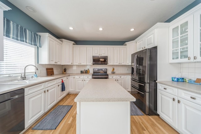 kitchen featuring a center island, light wood-type flooring, appliances with stainless steel finishes, white cabinets, and a sink