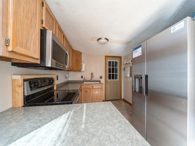 kitchen with appliances with stainless steel finishes, a textured ceiling, light countertops, and a sink