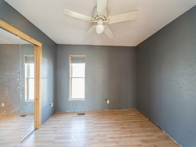 unfurnished room featuring visible vents, light wood finished floors, ceiling fan, a textured ceiling, and a textured wall