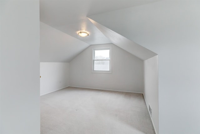 additional living space featuring visible vents, light carpet, baseboards, and vaulted ceiling