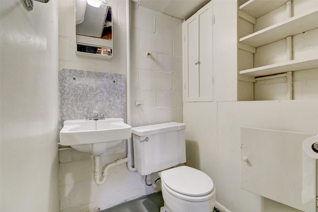 bathroom with toilet, concrete block wall, and a sink