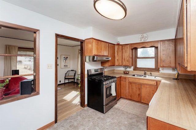 kitchen featuring brown cabinetry, stainless steel gas range, a sink, light countertops, and under cabinet range hood