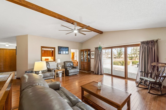 living area featuring a textured ceiling, lofted ceiling with beams, a ceiling fan, and wood-type flooring