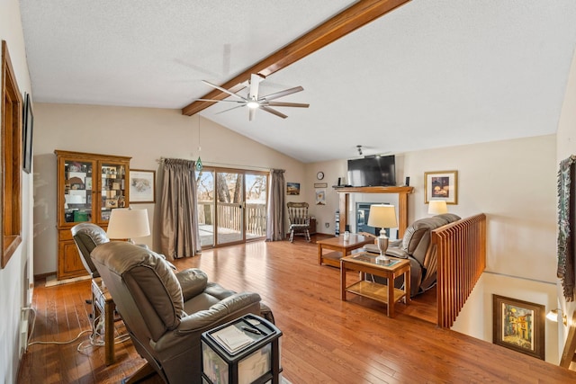 living room featuring lofted ceiling with beams, a textured ceiling, a glass covered fireplace, wood-type flooring, and ceiling fan