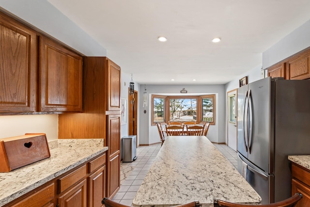 kitchen featuring light tile patterned floors, a kitchen island, recessed lighting, freestanding refrigerator, and brown cabinets