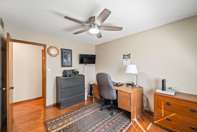 office space featuring wood finished floors, visible vents, baseboards, ceiling fan, and a textured ceiling