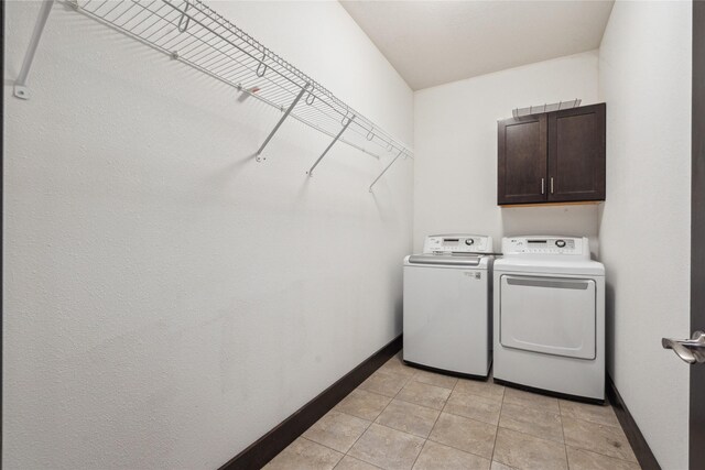 laundry room featuring washer and dryer, light tile patterned floors, cabinet space, and baseboards