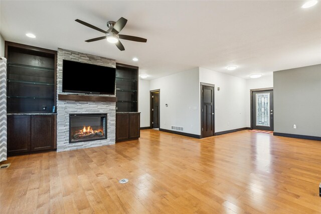 unfurnished living room with a ceiling fan, visible vents, baseboards, a fireplace, and light wood-style floors