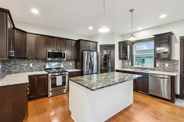 kitchen with light stone countertops, dark brown cabinetry, appliances with stainless steel finishes, light wood-style floors, and a sink