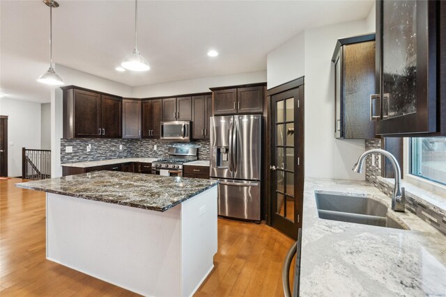 kitchen with light wood-type flooring, a sink, stainless steel appliances, dark stone counters, and dark brown cabinetry