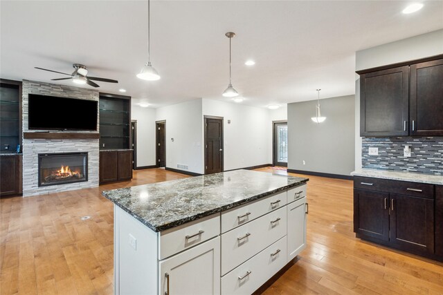 kitchen with open floor plan, dark stone counters, ceiling fan, and decorative backsplash