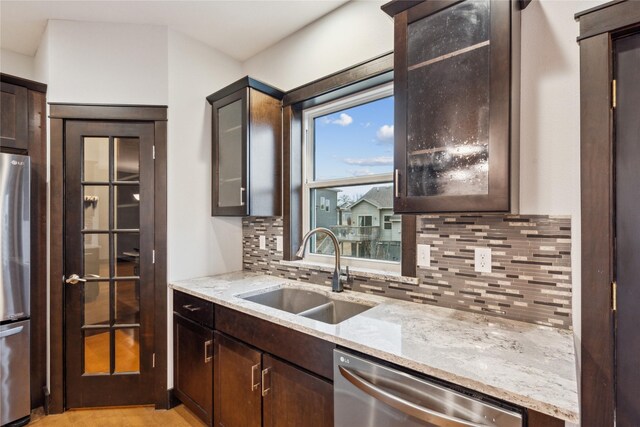 kitchen featuring light stone counters, dark brown cabinets, appliances with stainless steel finishes, and a sink