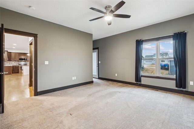 spare room featuring baseboards, light colored carpet, and ceiling fan