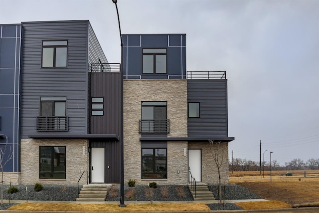 contemporary home featuring board and batten siding, a balcony, and stone siding