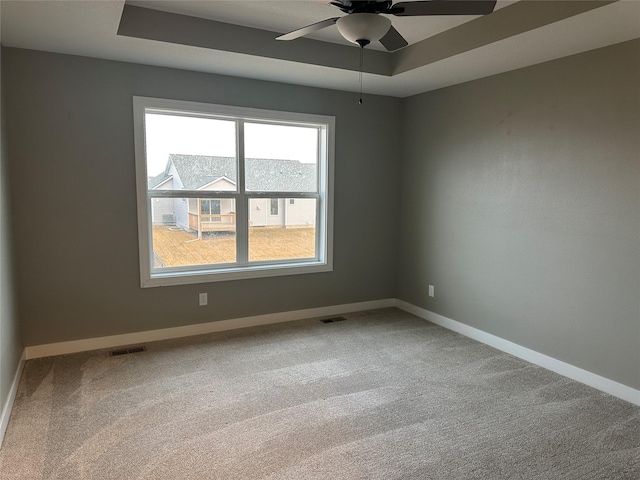 carpeted spare room with visible vents, a raised ceiling, and a ceiling fan