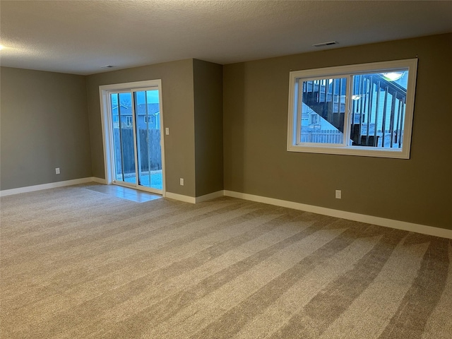 unfurnished room with carpet flooring, visible vents, baseboards, and a textured ceiling