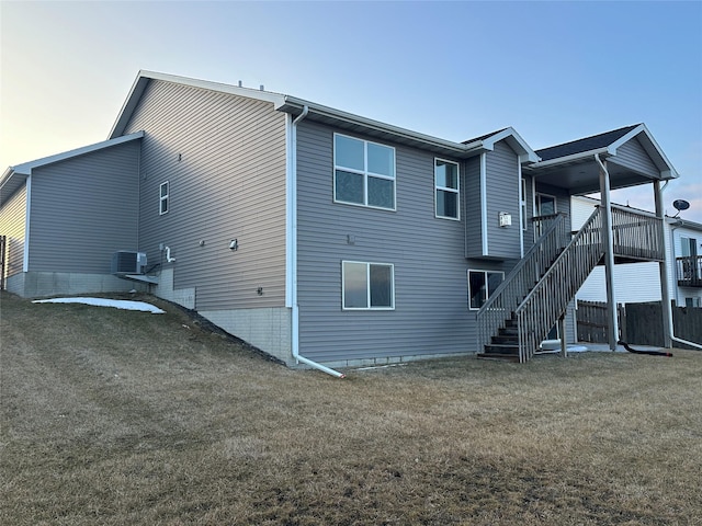 rear view of property with stairs, central air condition unit, and a yard