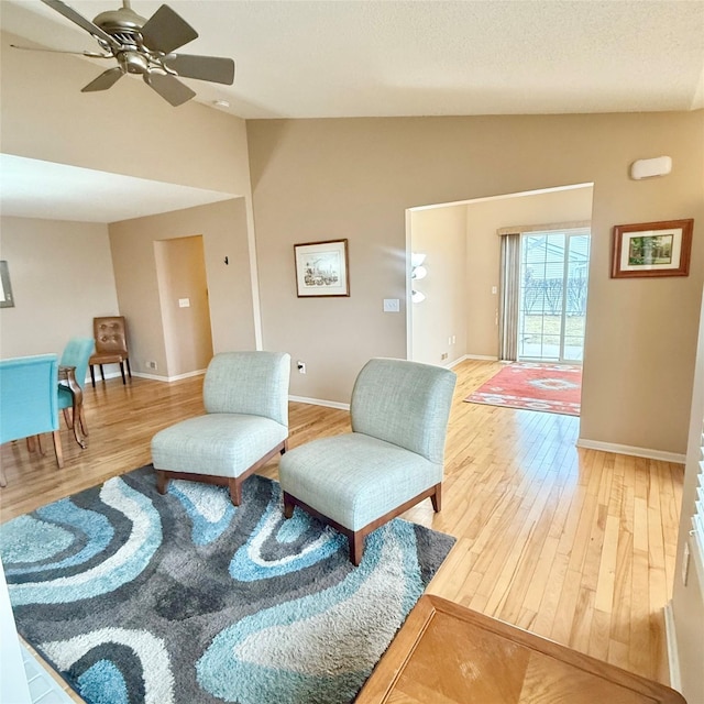 sitting room with a ceiling fan, a textured ceiling, light wood finished floors, baseboards, and vaulted ceiling