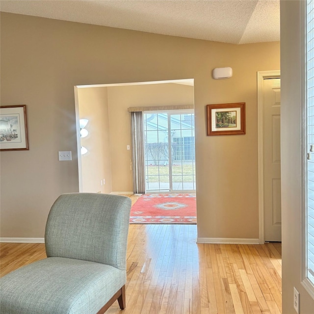 living area featuring light wood-style flooring, a textured ceiling, and baseboards