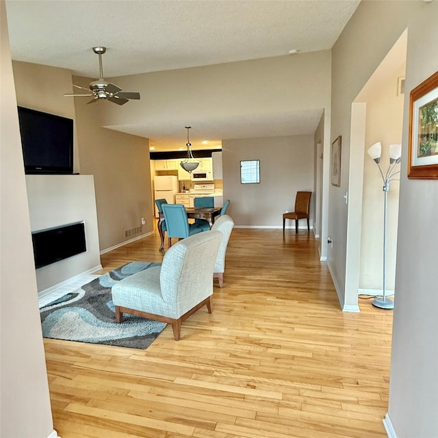 living room with baseboards, a fireplace, ceiling fan, a textured ceiling, and light wood-type flooring