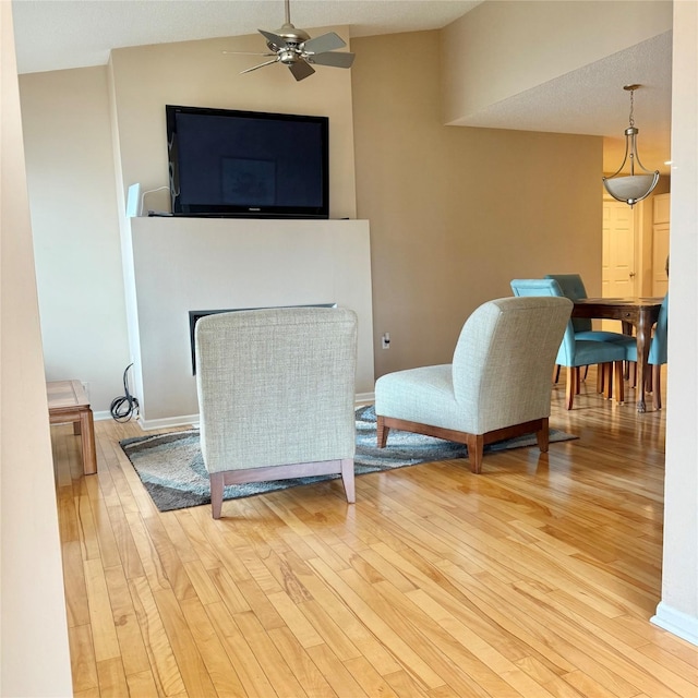 sitting room with light wood finished floors, baseboards, lofted ceiling, a fireplace, and a ceiling fan