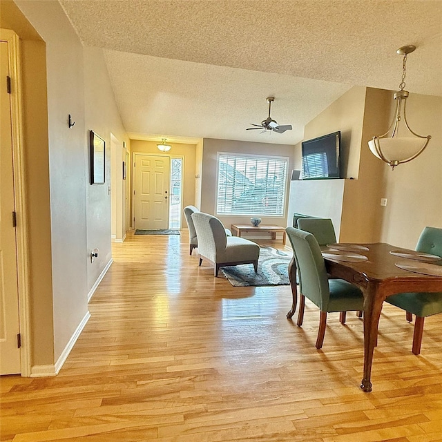 dining space with light wood finished floors, baseboards, ceiling fan, lofted ceiling, and a textured ceiling