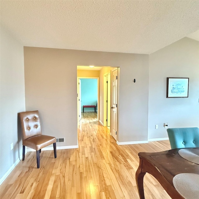 living area with light wood finished floors, visible vents, a textured ceiling, and baseboards