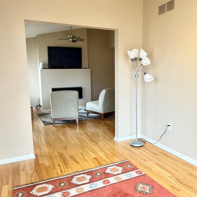 living area featuring visible vents, a ceiling fan, wood finished floors, a fireplace, and baseboards