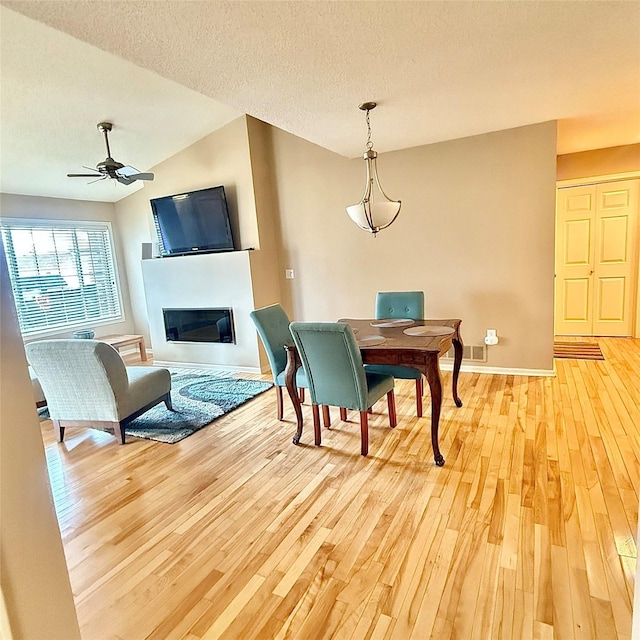 dining space featuring lofted ceiling, light wood-style flooring, ceiling fan, a textured ceiling, and a glass covered fireplace