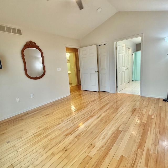 unfurnished bedroom featuring baseboards, visible vents, lofted ceiling, light wood-style flooring, and ensuite bathroom