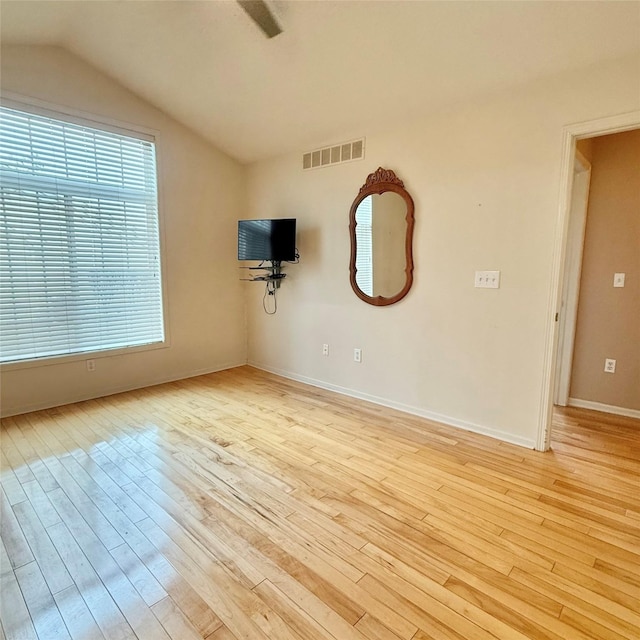 empty room with light wood finished floors, visible vents, baseboards, and lofted ceiling