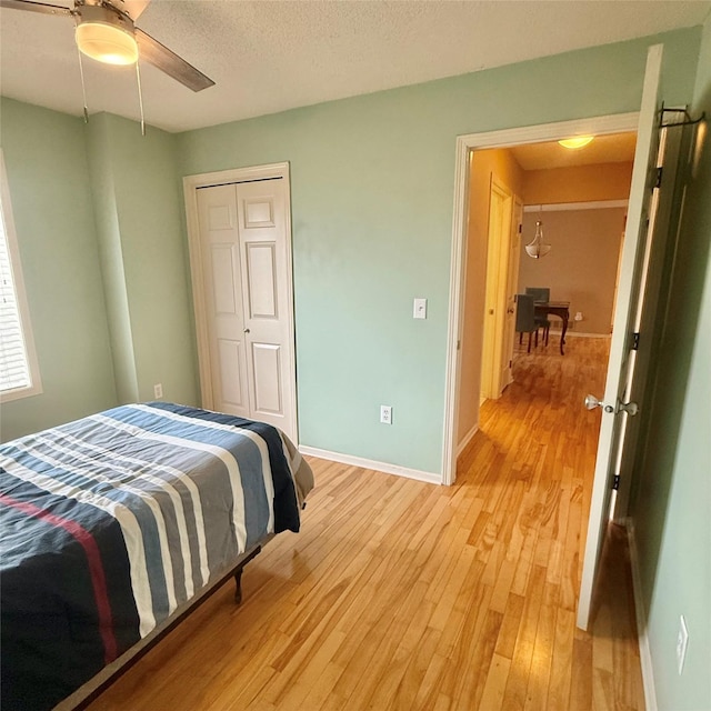 bedroom with light wood-type flooring, a textured ceiling, a closet, baseboards, and ceiling fan