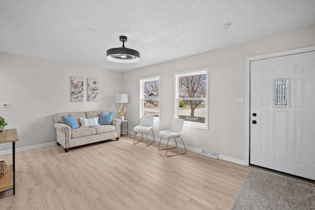 living area with light wood-type flooring, visible vents, and baseboards