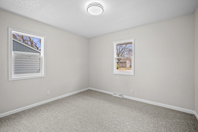 spare room featuring visible vents, baseboards, a textured ceiling, and carpet flooring