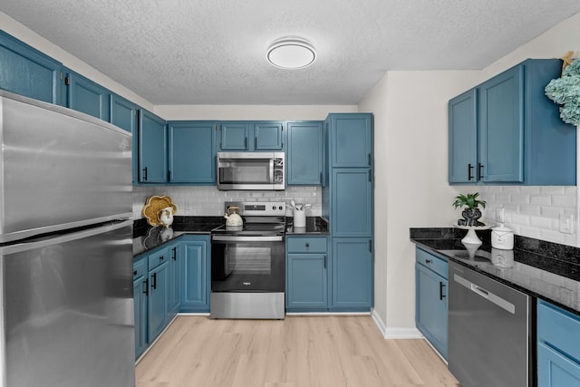 kitchen featuring light wood finished floors, blue cabinetry, stainless steel appliances, and dark stone counters