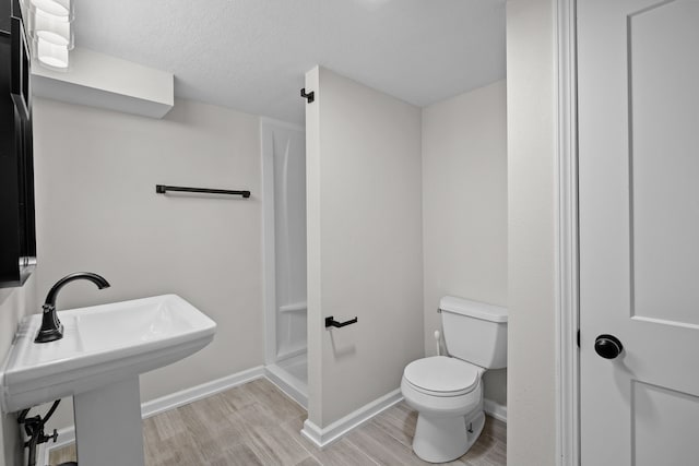 full bathroom featuring toilet, wood finished floors, a stall shower, and baseboards