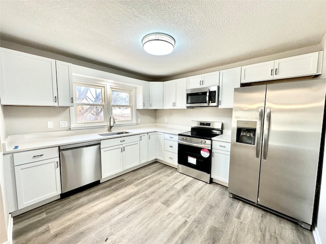 kitchen with light countertops, light wood-style flooring, white cabinets, stainless steel appliances, and a sink