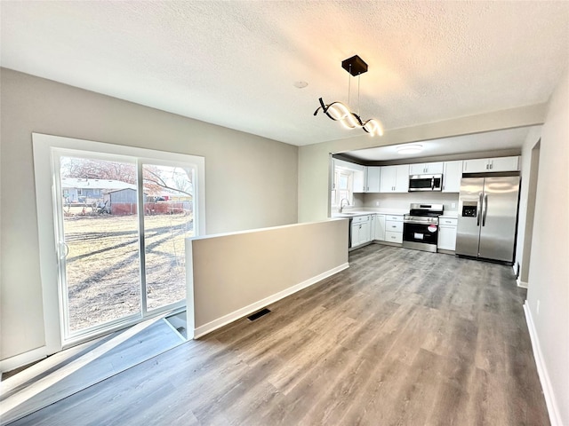 kitchen featuring pendant lighting, a sink, wood finished floors, appliances with stainless steel finishes, and light countertops