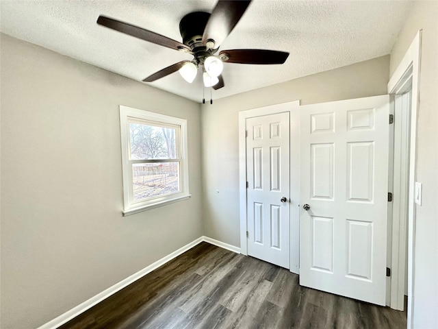 unfurnished bedroom with a closet, baseboards, a textured ceiling, and dark wood-style flooring