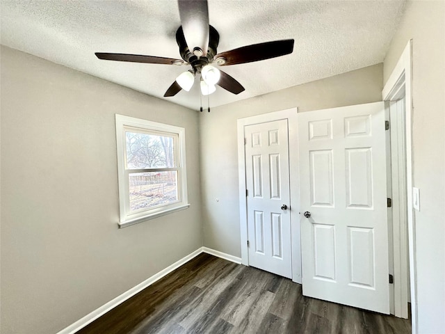 unfurnished bedroom with a closet, a textured ceiling, baseboards, and dark wood-style flooring