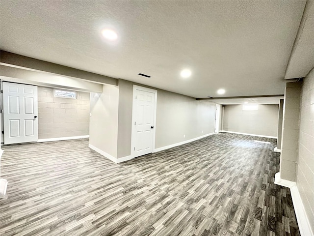 finished basement featuring a textured ceiling, concrete block wall, baseboards, and wood finished floors