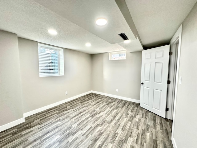 basement featuring baseboards, a textured ceiling, a healthy amount of sunlight, and wood finished floors