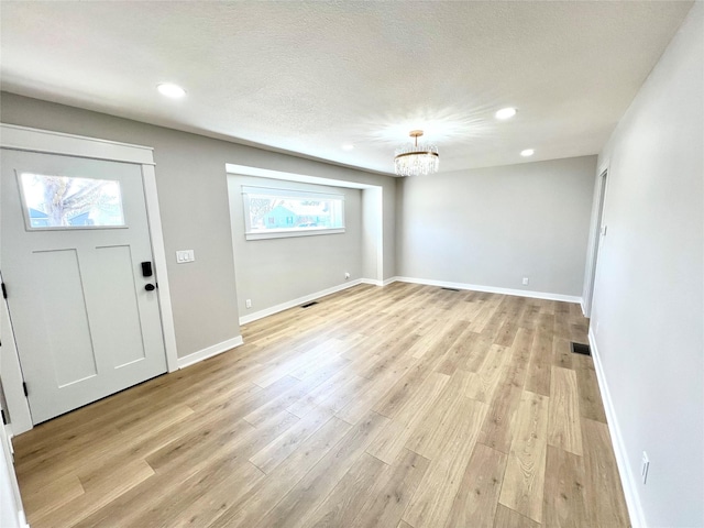 entryway with light wood finished floors, a chandelier, a textured ceiling, and baseboards