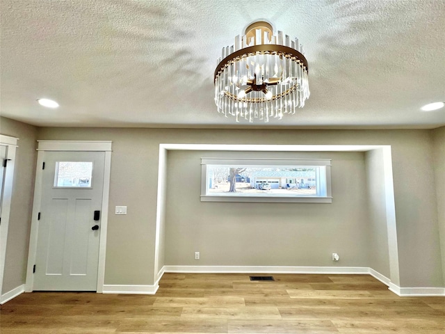 foyer entrance featuring a textured ceiling, wood finished floors, visible vents, and baseboards