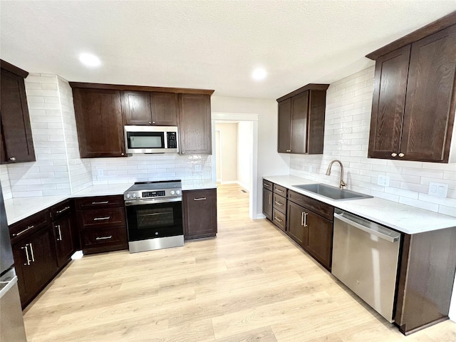 kitchen with a sink, stainless steel appliances, dark brown cabinetry, light countertops, and light wood-style floors