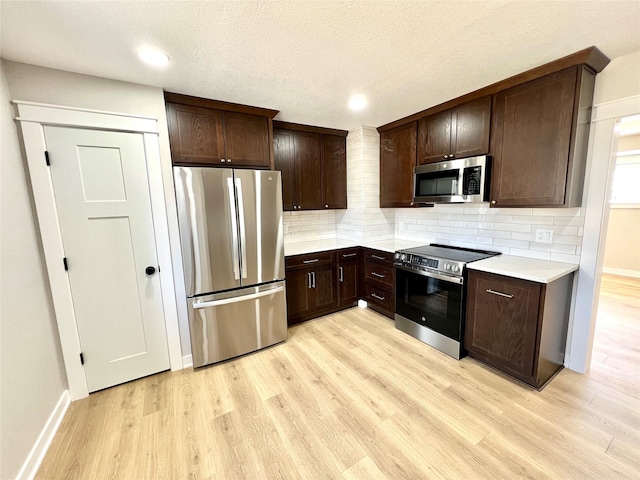kitchen with light countertops, light wood-style floors, dark brown cabinetry, tasteful backsplash, and appliances with stainless steel finishes