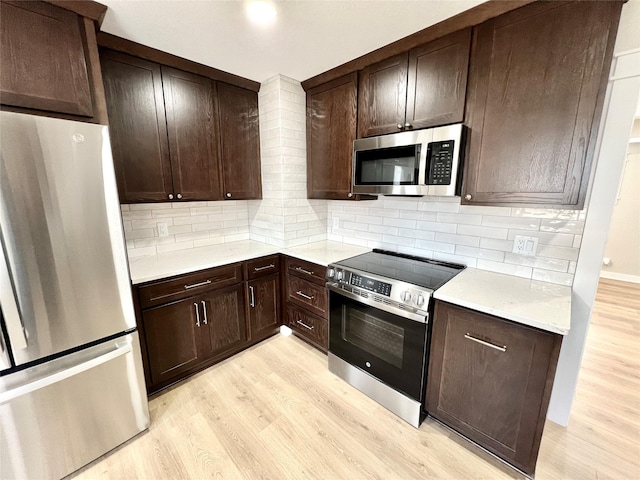 kitchen featuring light wood finished floors, backsplash, appliances with stainless steel finishes, and light countertops