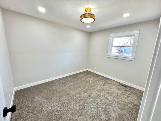 unfurnished room with visible vents, dark carpet, and baseboards